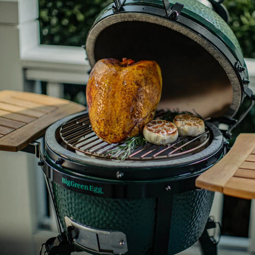 Big Green Egg grill with a roasted turkey and garlic on a wooden deck