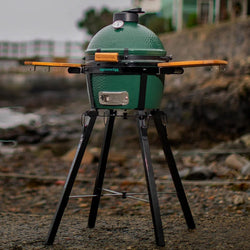 Green egg grill on a stand by a waterfront with houses in the background