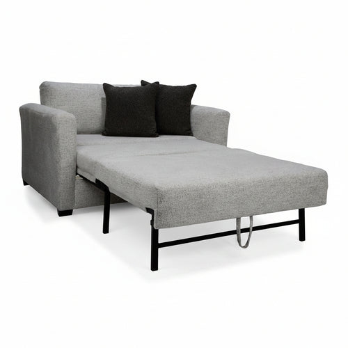 Gray sofa bed with black legs and two black pillows on a white background