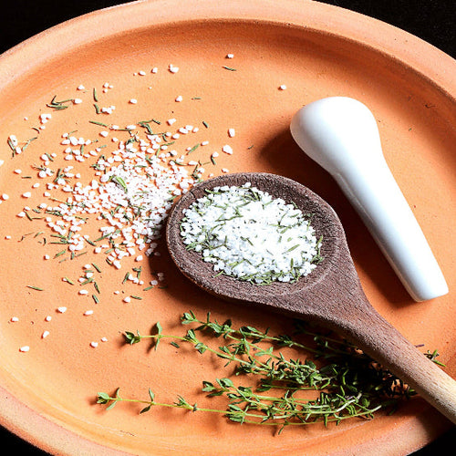 Terracotta plate with wooden spoon, white salt, and green herbs on a black background. Seasoning